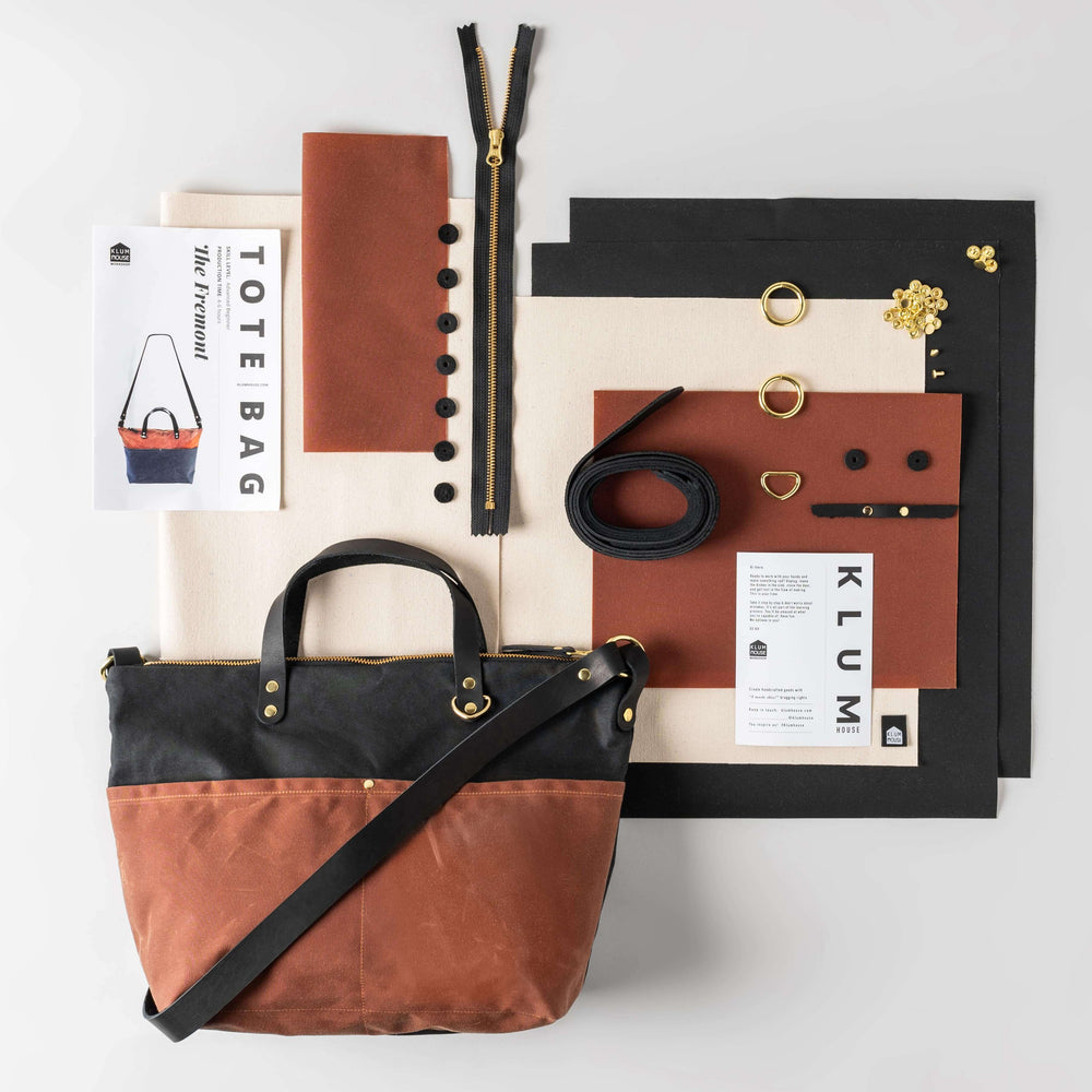The Fremont Tote maker kit laid out flat: black and rust waxed canvas, leather strap, brass hardware, zipper, and pattern booklet.