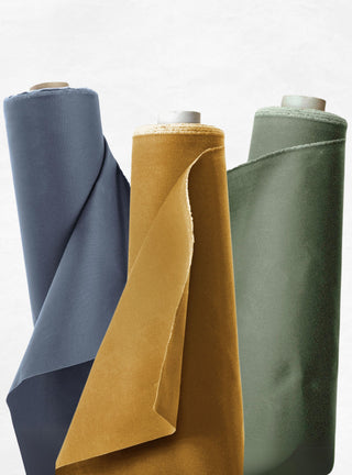 Rolls of waxed canvas standing on end in navy, mustard, and green.