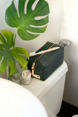 The Woodland Dopp Kit sitting in a bathroom besides the sink with a monstera plant next to it and a toothbrush on top of it.